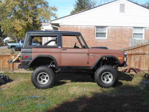 1972 Ford Bronco - A brown 1972 Ford Bronco sits on a grassy lawn in front of a house, showing its lifted suspension and aftermarket wheels.