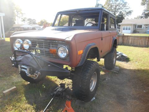 1972 Ford Bronco - first-generation Ford Bronco in primer/orange undergoing restoration, with a winch bumper, parked on a lawn.