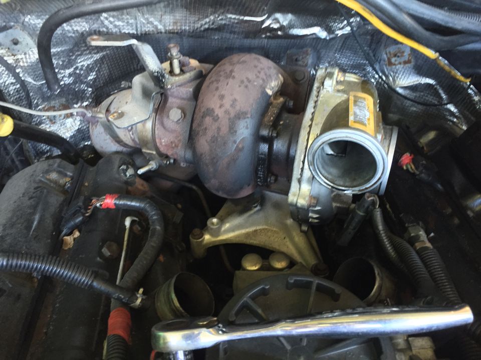 Turbocharger assembly with yellow label and visible engine parts. A wrench is in the foreground