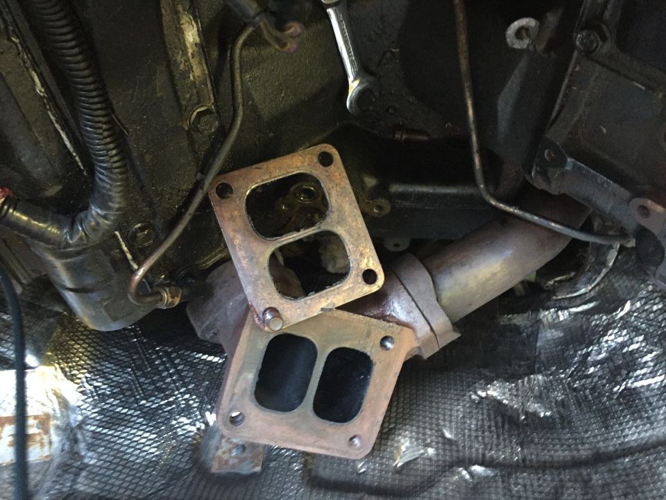 Two exhaust pipe flanges and a section of exhaust pipe, with engine components and wiring above