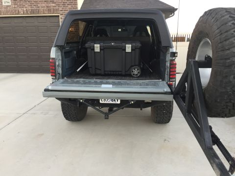 1988 Ford Bronco - Rear view of a gray Ford Bronco with its tailgate open, revealing a black storage box and a spare tire mount.