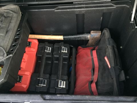 1988 Ford Bronco - A storage box contains various tools, including an axe and multiple tool cases, suggesting it is part of a vehicle's utility storage.