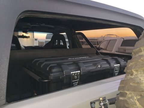 1988 Ford Bronco - A black storage box is visible inside a vehicle, with another vehicle seen through the window at sunset.