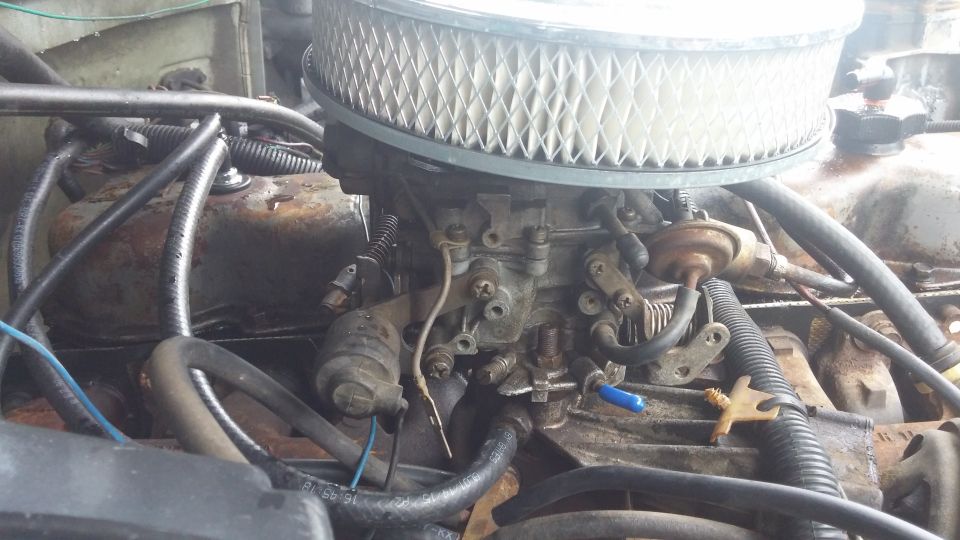 Engine carburetor with air filter, hoses, and wiring. Some rust and dirt visible
