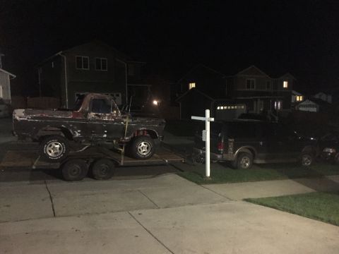 1978 Ford Bronco - Two vehicles are visible at night, one a pickup truck on a trailer, the other an SUV parked on the grass.