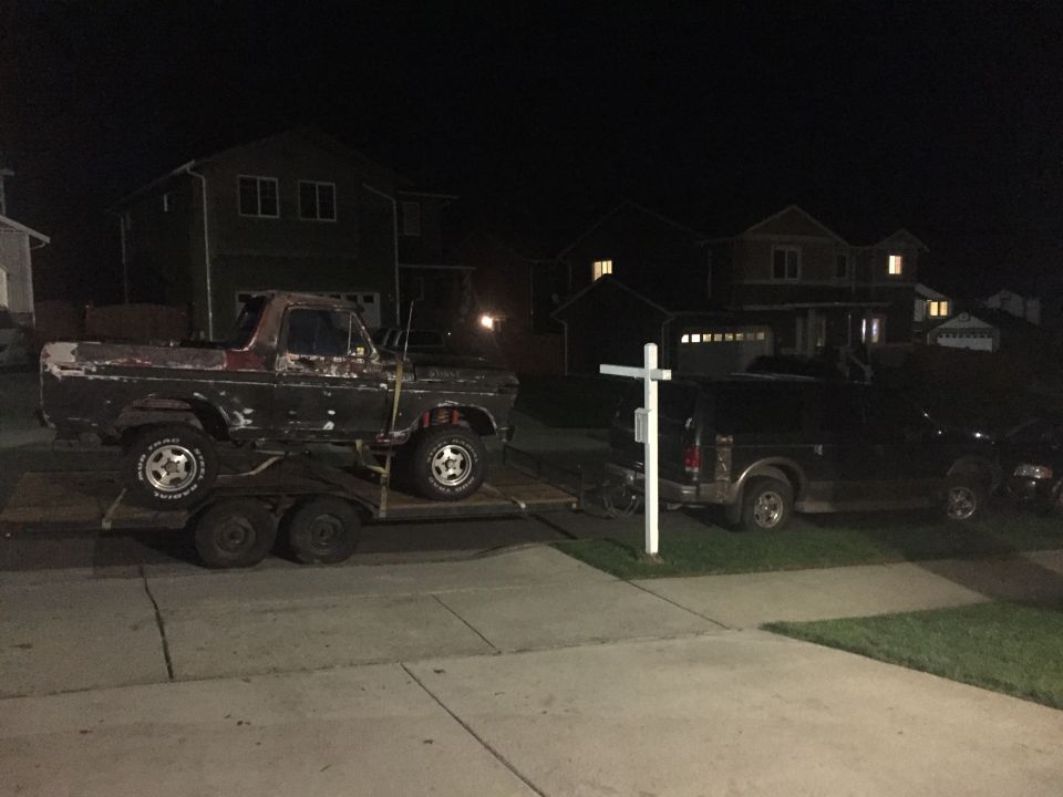 Old pickup truck on a trailer, another SUV parked nearby. Both vehicles are dark colored