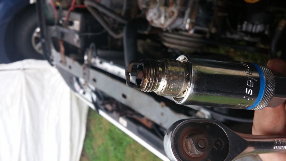 Spark plug with black deposits being removed from an engine with a socket wrench