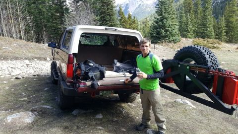 1996 Ford Bronco - A man stands by a 1996 Ford Bronco packed with gear, ready for an outdoor adventure in a mountainous area.