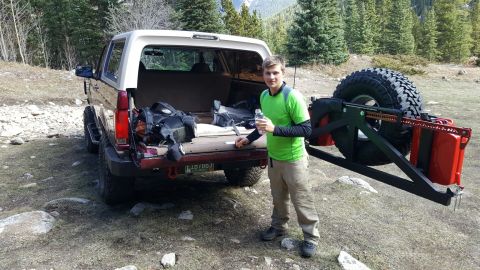 1996 Ford Bronco - A man stands next to a Ford Bronco loaded with gear in a wooded, mountainous area.