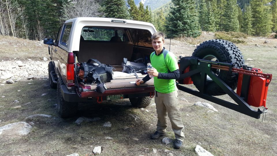 Brown and white Ford Bronco with open tailgate, spare tire carrier, and a man standing beside it