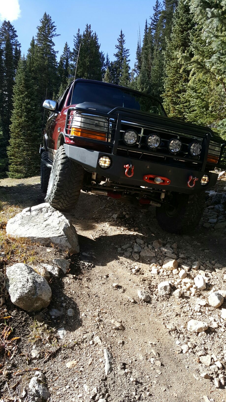 Red SUV with off-road tires and bumper driving over rocks on a dirt trail
