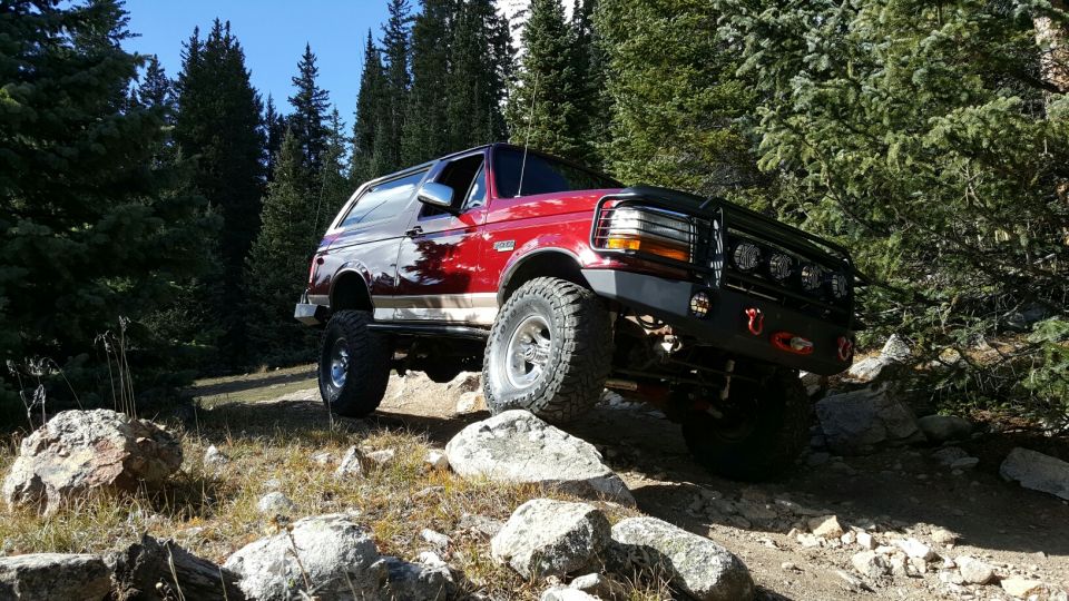 Red 1996 Ford Bronco with aftermarket bumper and lights navigating a rocky mountain trail