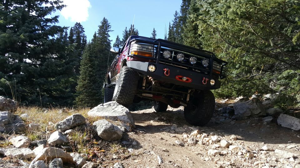 1996 Ford Bronco climbing over rocks on a mountain trail with trees in the background