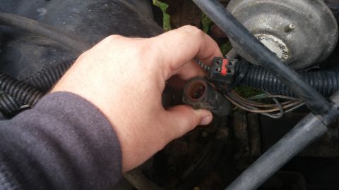 1984 Ford Bronco - A hand disconnects an electrical connector within the engine bay, showing engine components and wiring.