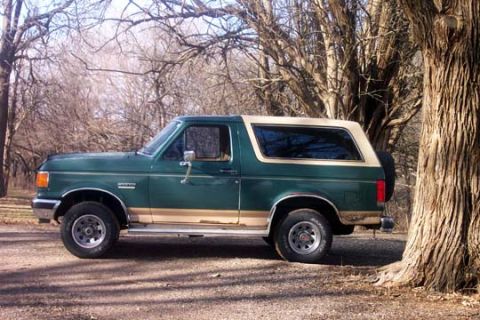 1987 Ford Bronco - Side view of a two-tone green and tan 1987 Ford Bronco, parked outdoors near trees.