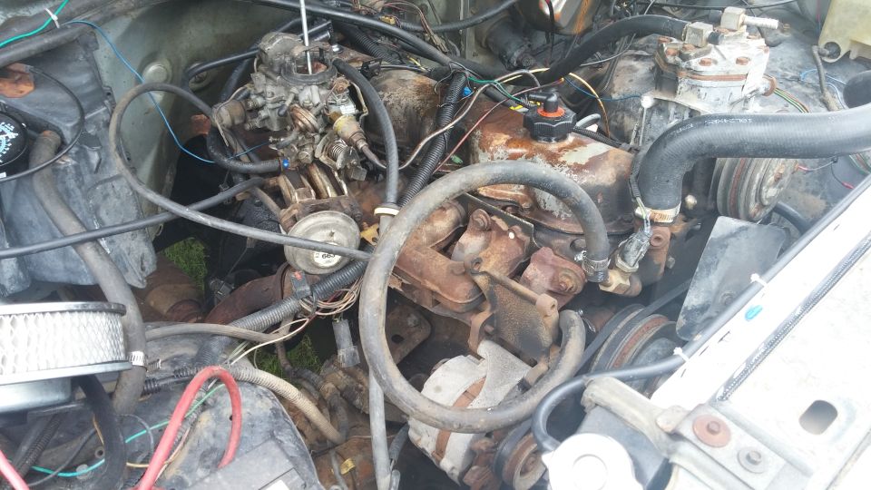 Engine bay with a V8 engine, carburetor, and air filter. Some rust is visible