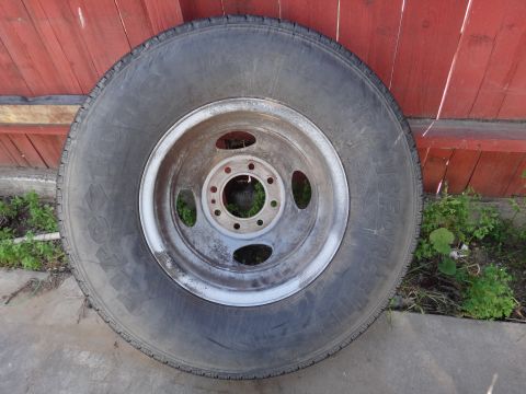 1995 Chevrolet P30 1 Ton - Step Van - A single tire and wheel assembly is shown resting against a wooden fence with some greenery around it.