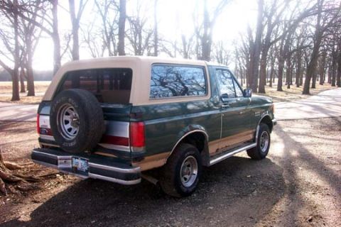 1987 Ford Bronco - A 1987 Ford Bronco is parked on a dirt road with trees lining the path.