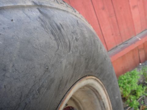 1995 Chevrolet P30 1 Ton - Step Van - A close-up view of a worn tire, showing cracks and tread detail against a red wooden wall.