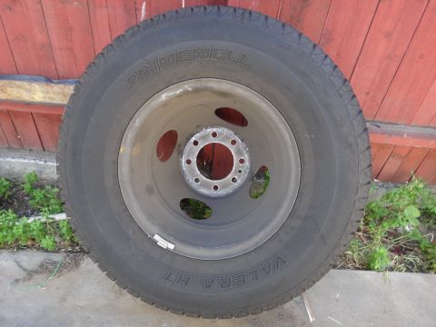 1995 Chevrolet P30 1 Ton - Step Van - A single truck wheel and tire assembly is shown against a wooden fence.
