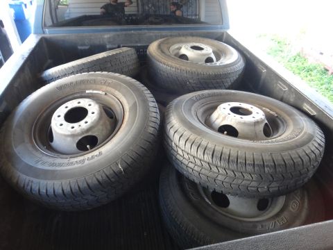 1995 Chevrolet P30 1 Ton - Step Van - Set of dirty steel wheels mounted with all-terrain tires stacked in the bed of a pickup truck.