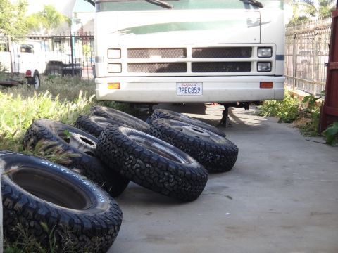 1995 Chevrolet P30 1 Ton - Step Van - Several off-road tires are laid out in front of a large RV or van, which is supported by jack stands.