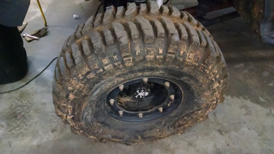 Muddy off-road tire on a black rim with a skull center cap. Tools are on the floor nearby
