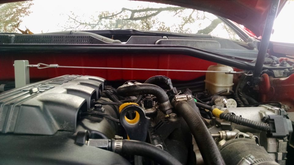 Close-up of an engine bay with various hoses and components visible. A white fluid reservoir is in the background