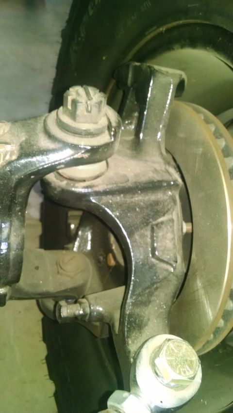 1985 Jeep CJ7 - A close-up view of the suspension and brake assembly of a vehicle, likely a Jeep CJ7, showing the steering knuckle, brake rotor, and tie ro…