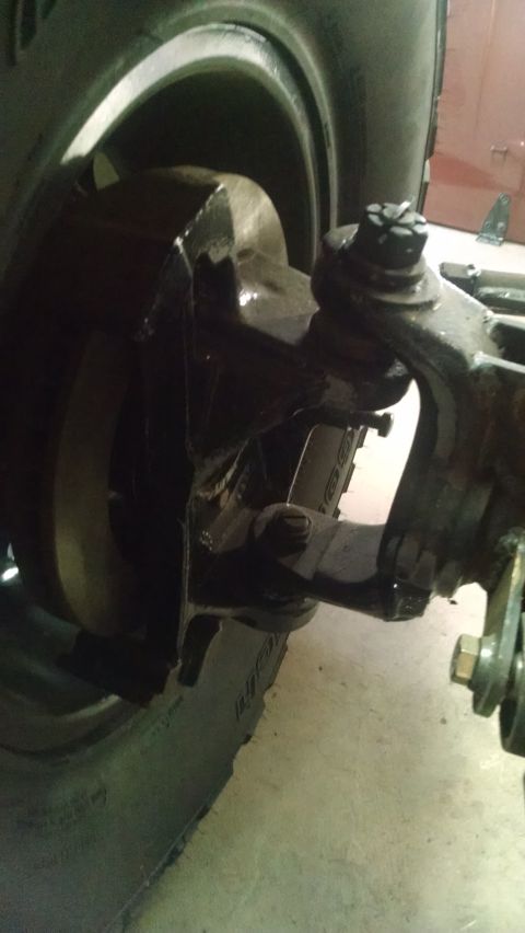 1985 Jeep CJ7 - A close-up view of the front suspension and brake assembly of a Jeep CJ7, showing the steering knuckle, brake rotor, and part of the tire.