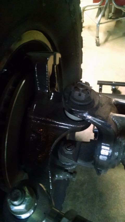 1985 Jeep CJ7 - A close-up view of the suspension and steering components of a vehicle, likely a Jeep CJ7, showing a black painted steering knuckle, tie ro…