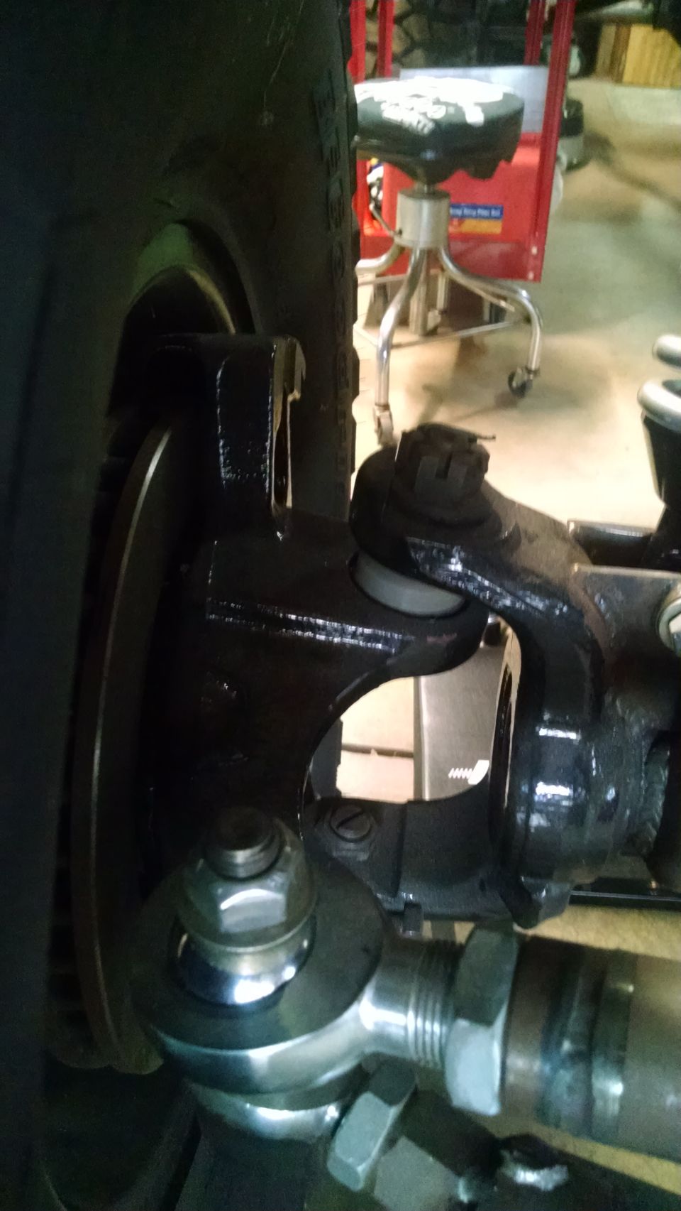 Close-up of vehicle suspension and steering parts, including tire, brake rotor, tie rod end, and ball joint.