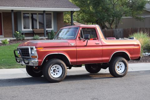 1978 Ford Bronco - A red 1978 Ford Bronco is parked on a paved street in front of a house. The vehicle has a chrome bumper with a black brush guard and off-ro…