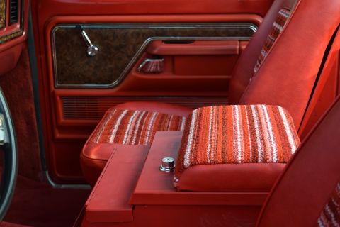1978 Ford Bronco - The interior of a vintage Ford Bronco features red vinyl seats and door panels, with a patterned fabric on the center console lid and seat…