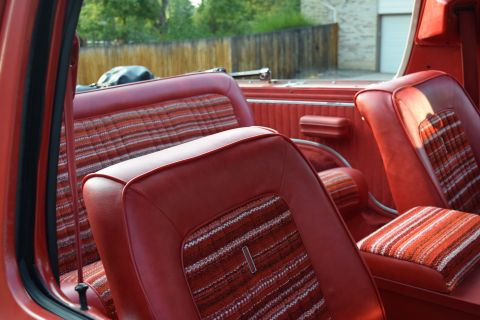 1978 Ford Bronco - The interior of a vintage Ford Bronco shows red vinyl seats with striped fabric inserts. The view is from the driver's side, looking toward…