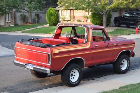 1978 Ford Bronco - The rear passenger side view of a red 1978 Ford Bronco with orange and yellow pinstripes, parked on a residential street. The vehicle has a…
