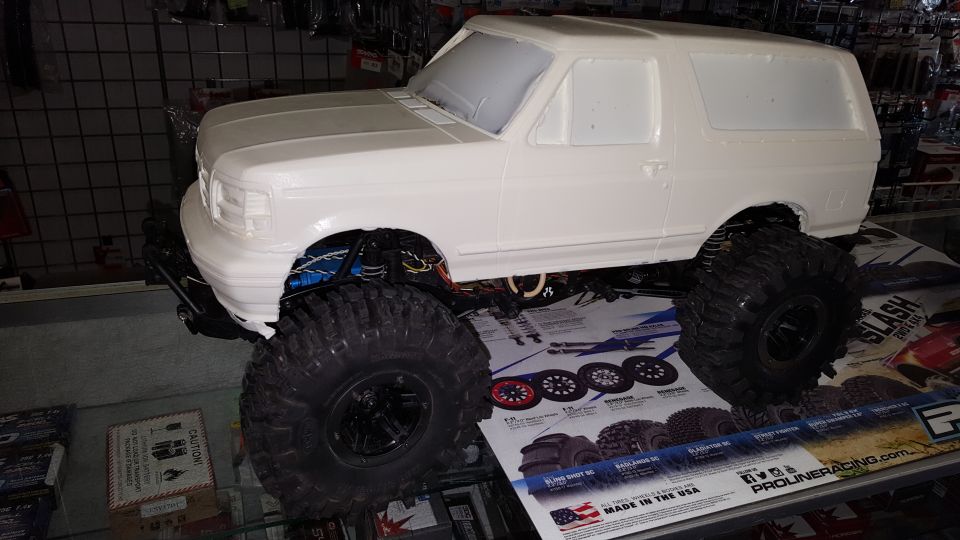 White unpainted RC crawler Bronco body on a chassis with coilovers and knobby crawler tires