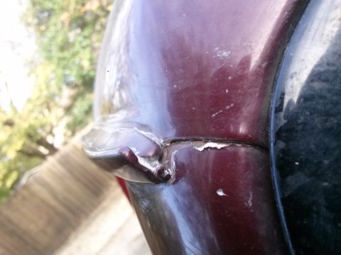 1996 Ford Bronco - A close-up view shows damage to the maroon paint on a vehicle's rear quarter panel, near the wheel well. The paint is cracked and peeling,…