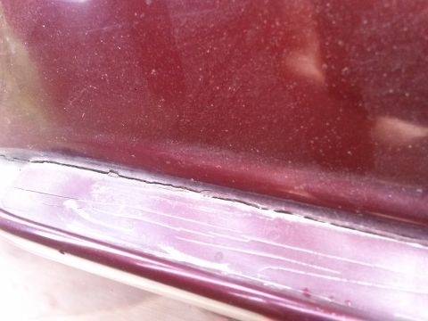 1996 Ford Bronco - A close-up view of the lower body panel of a dark red vehicle, showing a cracked and peeling trim piece along the bottom edge.