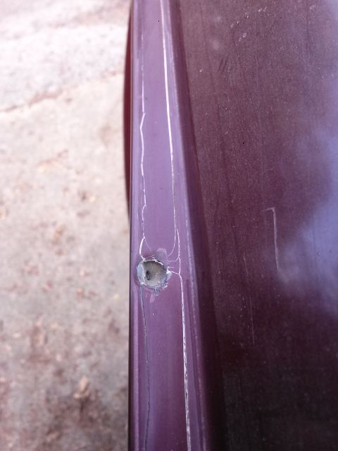 1996 Ford Bronco - A close-up shot shows a hole with surrounding cracks on a dark purple vehicle panel. The panel appears to be part of the exterior body, pos…