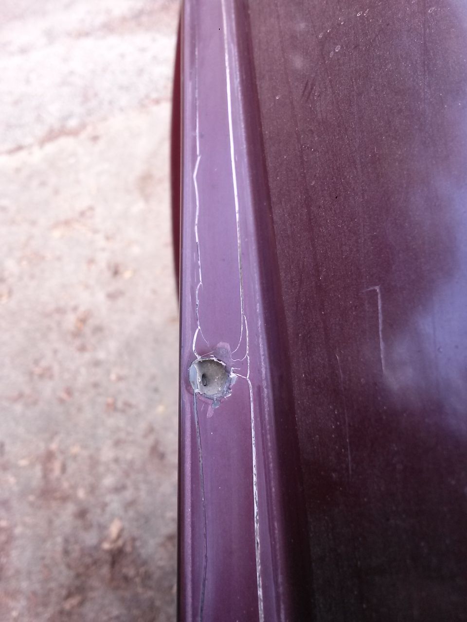 Close-up of a hole and cracks on a dark purple vehicle panel.