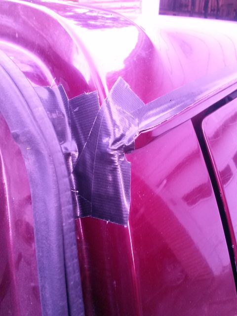 1996 Ford Bronco - A close-up view of a red vehicle's roofline shows a makeshift repair using black duct tape on the drip rail.