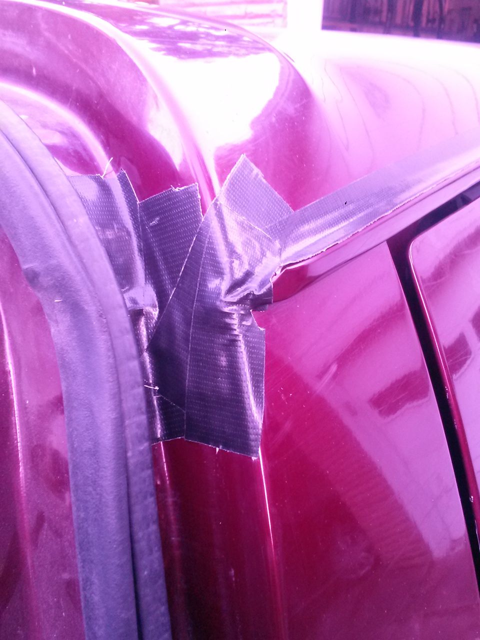 Red vehicle roofline with a black duct tape repair on the drip rail