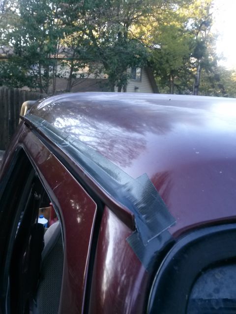 1996 Ford Bronco - The maroon paint of a 1996 Ford Bronco is visible, with a section of the roof and driver's side door frame showing. Black duct tape is appl…