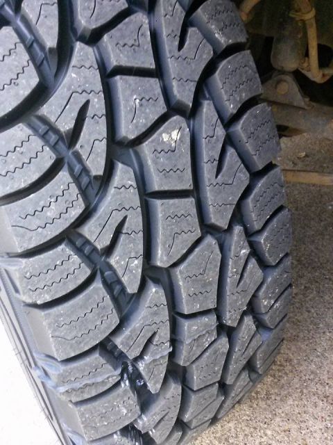 1996 Ford Bronco - A close-up, angled view of a tire tread on a vehicle. The tire has a deep, aggressive tread pattern with sipes and large blocks, suggesting…