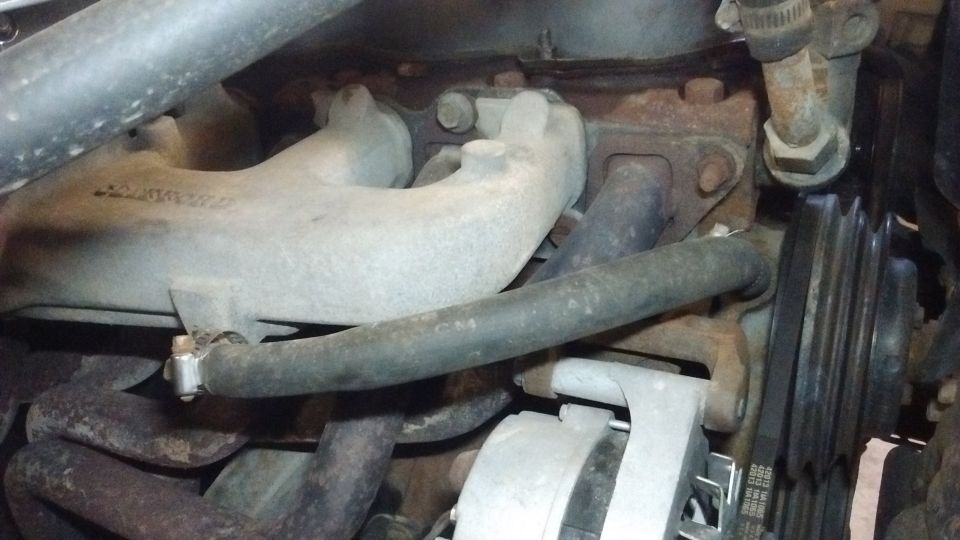 1985 Ford Bronco engine bay: exhaust manifold, hoses, alternator, and pulley system.