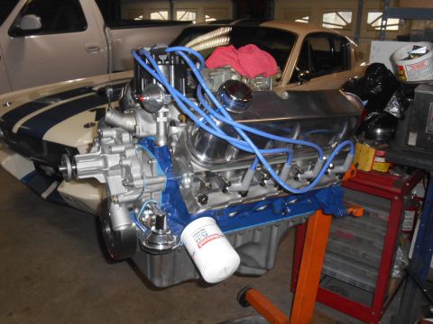 1972 Ford Bronco - A V8 engine with blue spark plug wires and a chrome valve cover is mounted on an engine stand. The engine is partially installed in a class…
