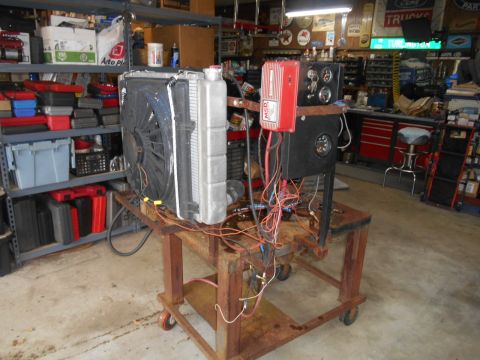 1972 Ford Bronco - A radiator and fan assembly are mounted on a rusty metal cart, connected to an MSD ignition box and gauges. The assembly is in a cluttered…