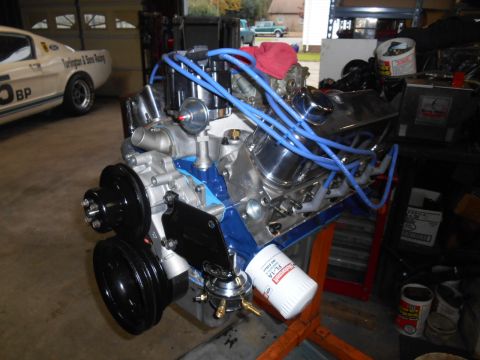 1972 Ford Bronco - A rebuilt V8 engine with blue spark plug wires and a chrome valve cover sits on an orange engine stand. A white Ford Mustang with racing st…
