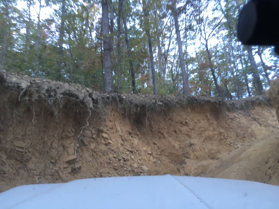 Dirt embankment with tree roots and a white surface in the foreground.